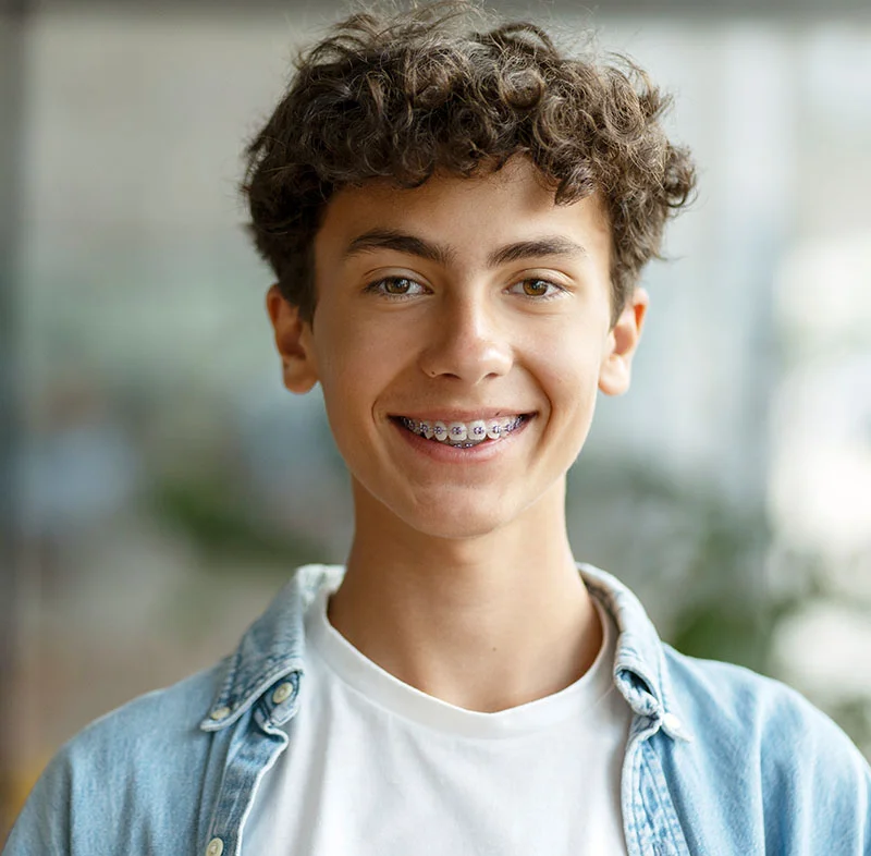 A young boy with curly hair, smiling with braces- Teen Dental Care in Fort Lee, NJ